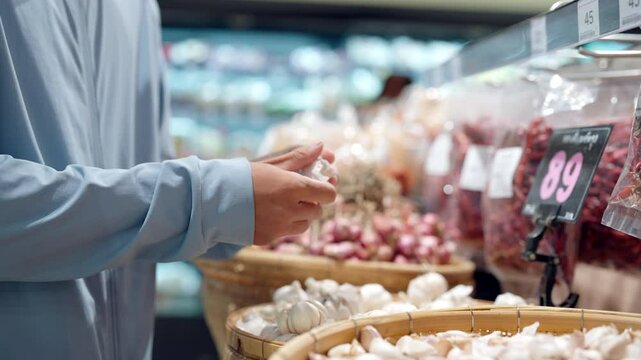A man is holding a bag of garlic in a grocery store. The store is filled with various items, including a basket of garlic