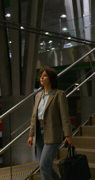 A stylish woman with a briefcase goes down to the railway platform. Dimmed lights. Metro station
