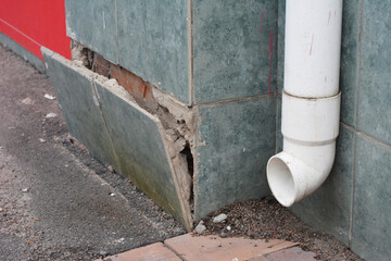 House foundation facing wall damage details from frost and wetness. House plinth foundation problem caused by damp from rain gutter downspout pipe.