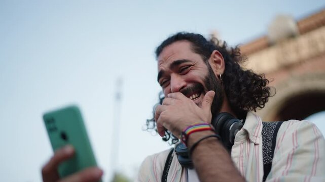 Happy Hispanic Man enjoying carefree moment while using  mobile phone device, embracing joy of travel. Sharing photos in social media and reading comments from followers on mobile app
