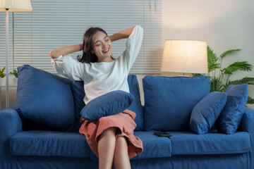 Obraz premium Beautiful smiling Asian woman sitting and relaxing Relax happily at home on the sofa. Watching TV in the living room at home on the weekends. Lifestyle concept.