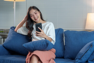 Obraz premium Cheerful Asian woman using mobile phone Chat on the website, application, download, work or study online. Sit on the sofa and relax. modern technology concept