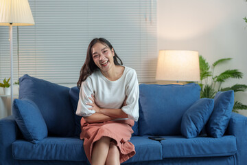 Obraz premium Beautiful smiling Asian woman sitting and relaxing Relax happily at home on the sofa. Watching TV in the living room at home on the weekends. Lifestyle concept.