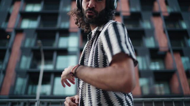 Smiling young man in headphones extends hand playfully, inviting viewers to join him in dance.charismatic expression and welcoming gesture create lively engaging moment, spreading joy and connection
