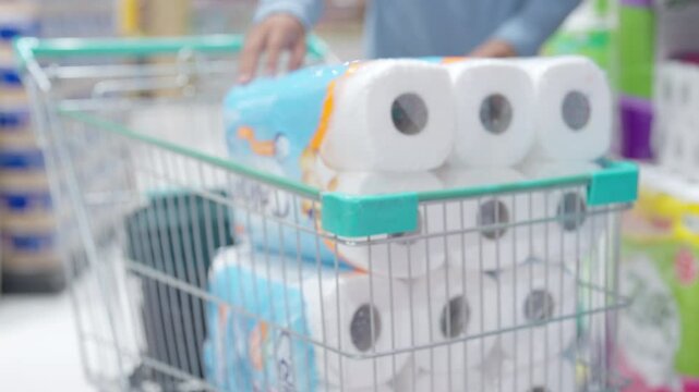 A person is reaching for a pack of toilet paper. Concept of urgency and necessity, as toilet paper is a basic household item that people need to have on hand