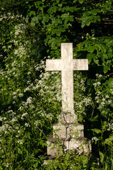 White stone cross memorial in old churchyard situated in bushes with wild flowers.