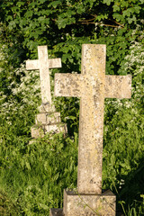 Two old weathered white stone Christian crosses standing in old cemetery surrounded by greenery