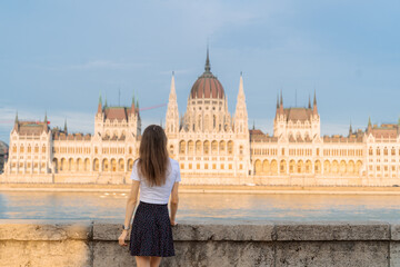 Fototapeta premium Tourism in Europe. Back view of young woman enjoying view of Hungarian Parliament Building on Danube River in Budapest, Hungary.