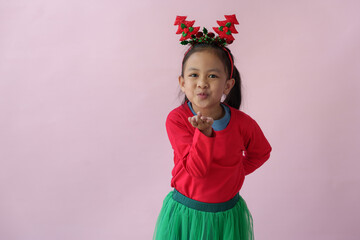 Adorable little Asian girl with Christmas tree headband, antlers showing various poses, standing, smiling, laughing, having fun in various poses, pink background. Holiday concept annual festival.