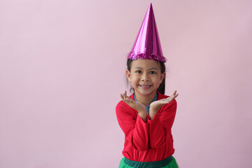 Adorable little Asian girl with a party hat showing various action poses, standing, smiling, dancing, laughing, and having fun in various poses, pink background. Holiday concept annual festival.