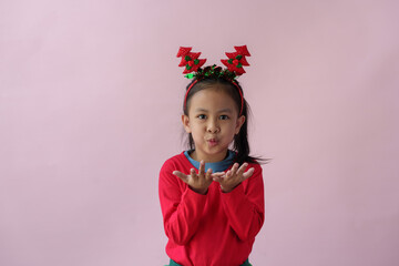 Adorable little Asian girl with Christmas tree headband, antlers showing various poses, standing, smiling, laughing, having fun in various poses, pink background. Holiday concept annual festival.