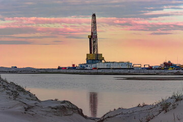 Fototapeta premium Drilling oil and gas wells in desert terrain. Sand hills, sparse vegetation. Beautiful sky. Infrastructure of the drilling rig