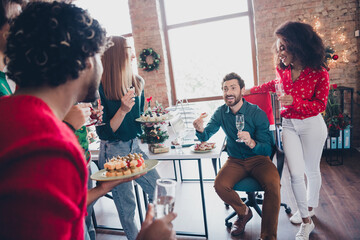 Photo of cheerful young people colleagues eat snacks champagne have fun cozy christmas party decor spacious office indoors