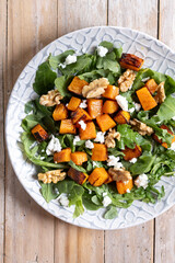 Pumpkin salad with arugula, walnuts and feta cheese on wooden