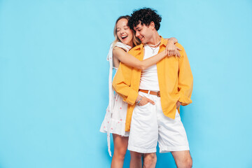 Happy beautiful romantic teenage couple. Smiling handsome caucasian man and young woman in summer clothes posing in studio, hugging sharing emotions, cheerful and happy. Isolated on blue