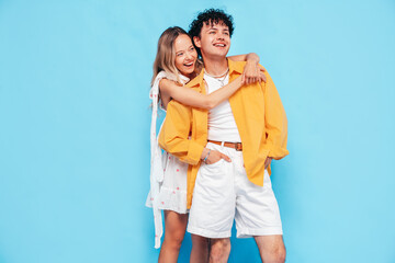 Happy beautiful romantic teenage couple. Smiling handsome caucasian man and young woman in summer clothes posing in studio, hugging sharing emotions, cheerful and happy. Isolated on blue