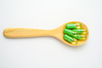 transparent capsules pills with a mixture of green powder and oil in wooden spoon, vitamin supplements