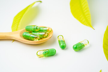 transparent capsules pills with a mixture of green powder and oil in wooden spoon, vitamin supplements