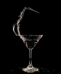 Cocktail Glass with splashing water alcohol, Crystal Cocktail drink splatter splash in air and bubble from glass. Liquor Part freeze shot high speed over black background isolated