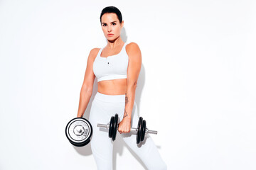 Fitness confident woman in white sports clothing. Sexy young beautiful model with perfect body. Female isolated on white wall in studio. Stretching out before training. Making exercises with dumbbells