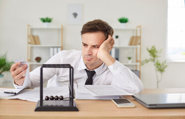 Grumpy bored overworked businessman looking unhappily at stack of paper work, sitting at work desk...