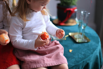 Anticipating Christmas: A Citrus Celebration. two little girls sitting in front of a beautifully decorated Christmas tree, eagerly peeling mandarins in anticipation of the holiday festivities.