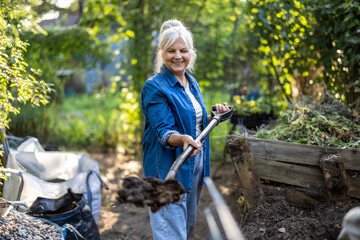 Senior woman shoveling compost heap in her garden
