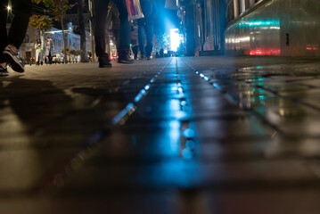 A rainy night in the city, with shop window reflections shimmering on the wet pavement. People silhouettes