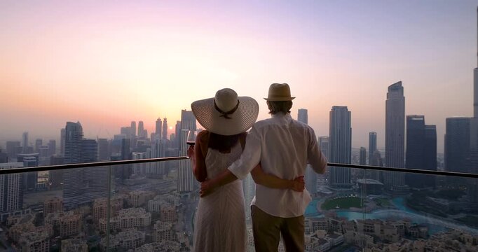 A hugging tourist couple enjoys the romatic sunset behind the skyline of Downtown Dubai, UAE