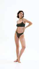 Obraz premium Full-body photo of young attractive woman posing elegantly dressed in dark green underwear against white studio background. Concept of spa procedure, self-care treatments, self-love, fashion and style