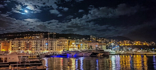 Reflets de lumières et de couleurs chaudes lors d'une pleine lune sur le port Lympia à Nice sur la Côte d'Azur avec des bateaux, des yachts et de beaux bâtiments colorés