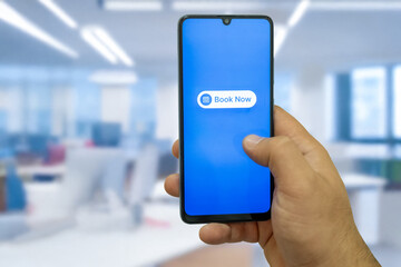 Close-up of the “Book Now” message on the smartphone screen. Online booking concept. Office background. Early booking message. 