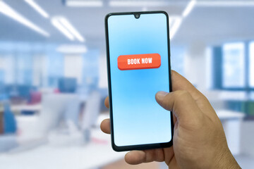 Close-up of the “Book Now” message on the smartphone screen. Online booking concept. Office background. Early booking message. 