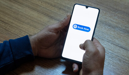 Close-up of the “Book Now” message on the smartphone screen. Online booking concept. Office background. Early booking message. 