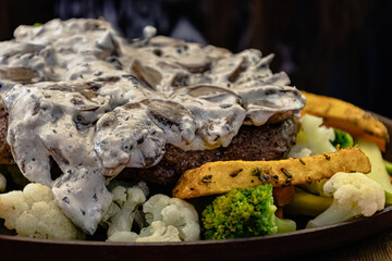 Close-up view of beef steak served with mushroom sauce, fries and grilled vegetables