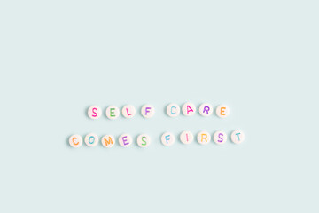 Self care comes first. Quote made of white round beads with multicolored letters on a blue background.