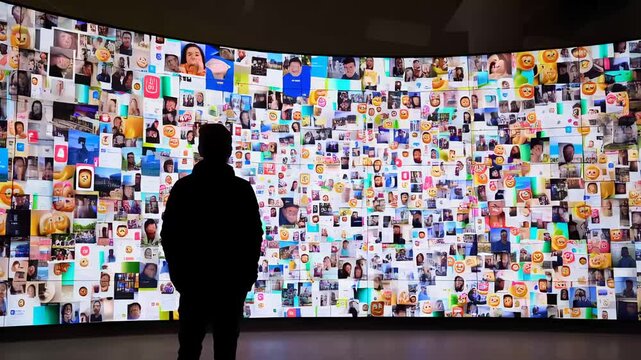 A man stands before a large, curved video wall displaying a multitude of images and videos. A visual representation of information overload or digital media.