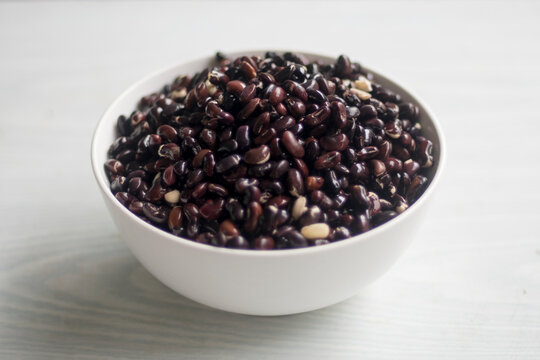 Black beans or black grams or Urad beans, after soaked 12 hrs., in a white bowl isolated on white table closeup selective focus. Preparation for cooking in kitchen