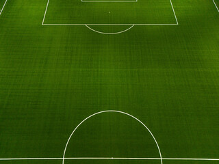 Green grass and white lines. Aerial closeup of the midfield circle and goal lines in an empty natural grass football field. Here the kick off is taken in a game of soccer.
