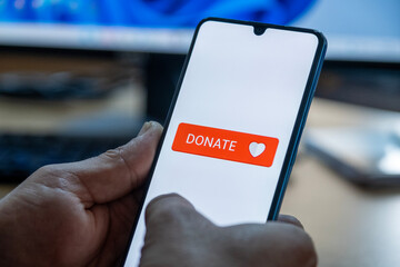 Close-up of “Donate” message on smartphone screen. Online donation concept. Office background. Donate message. 