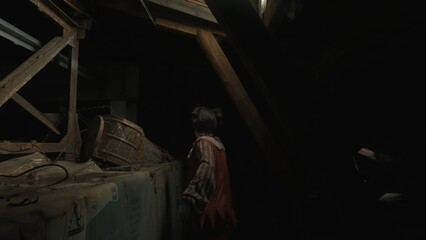 Crazy creepy killer man dressed as clown with makeup walking at attic in ruined house, back view shot. Halloween thriller concept.