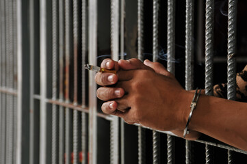 hands of a prisoner behind prison bars on black background	
