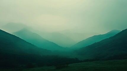 Fototapeta premium A misty, green mountain range in the distance with a field in the foreground.