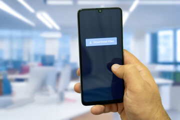 Close-up of “Download” message on smartphone screen. Online file download concept. Office background. Download message. 