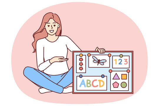 Woman english teacher in elementary school with magnetic board with alphabet and geometric shapes. Girl is sitting on floor explaining rules of english language to young children in accessible way.