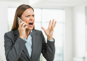 Angry businesswoman yelling on the phone in a modern office setting during daylight hours