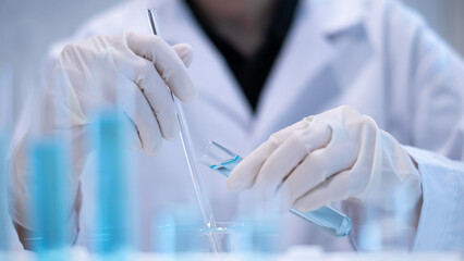 Close-up scientist pouring blue liquid into test tube beaker flask equipment pipette working laboratory experiment research chemical biology discovery healthcare and medicine accuracy solution © Supapich