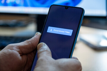 Close-up of “Download” message on smartphone screen. Online file download concept. Office background. Download message. 