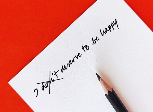 Paper on red background with handwritten text - I don't deserve to be happy - change to I deserve to be happy - to overcome negative self-talk or inner dialogue and believe in yourself