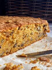 Carrot sponge cake, cut in half, shows off the texture: grated carrots, walnuts, moist crumb. Sponge crumbs and a knife nearby